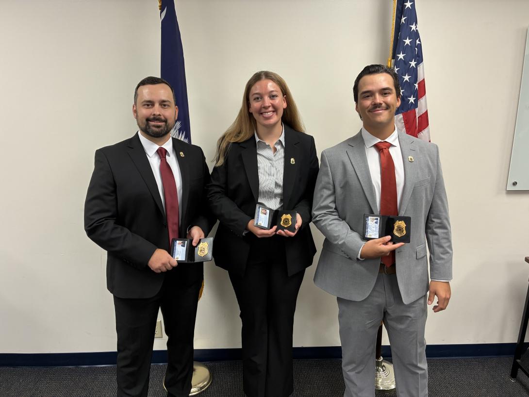 A group of three people smiling and holding badges.