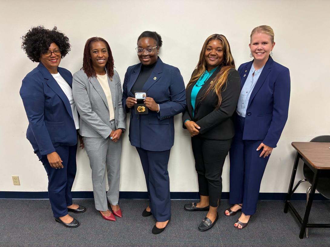 A newly graduated agent stands with agency leadership after completing the Criminal Justice Academy.